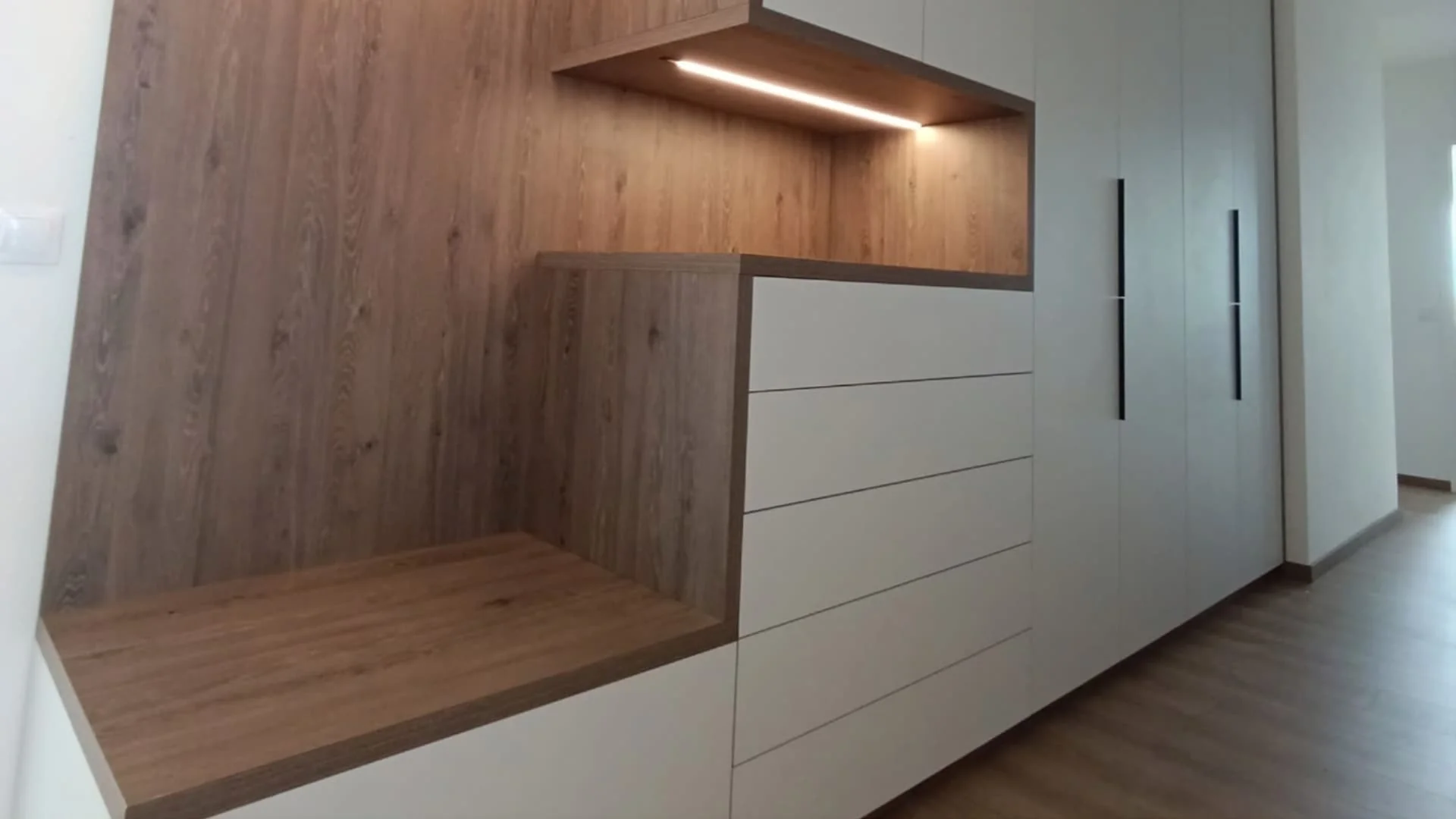 Vestavěná bílá skříň na chodbě s dřevěnou lavicí a LED podsvícenou nikou